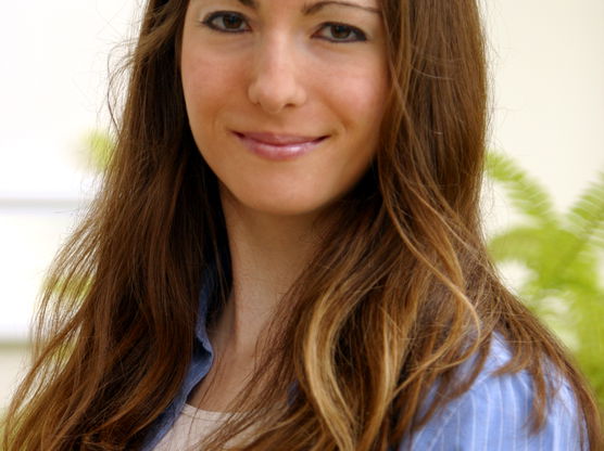 Portrait of a smiling woman with long brown hair wearing a light blue, striped shirt over a white top.