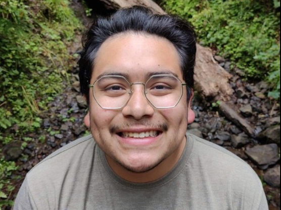 A portrait of Nathan standing in a forest with a closeup on his face. 