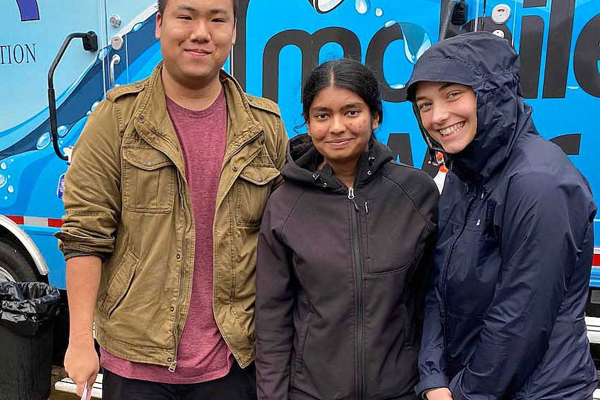 Students standing in front of a blue bus. 