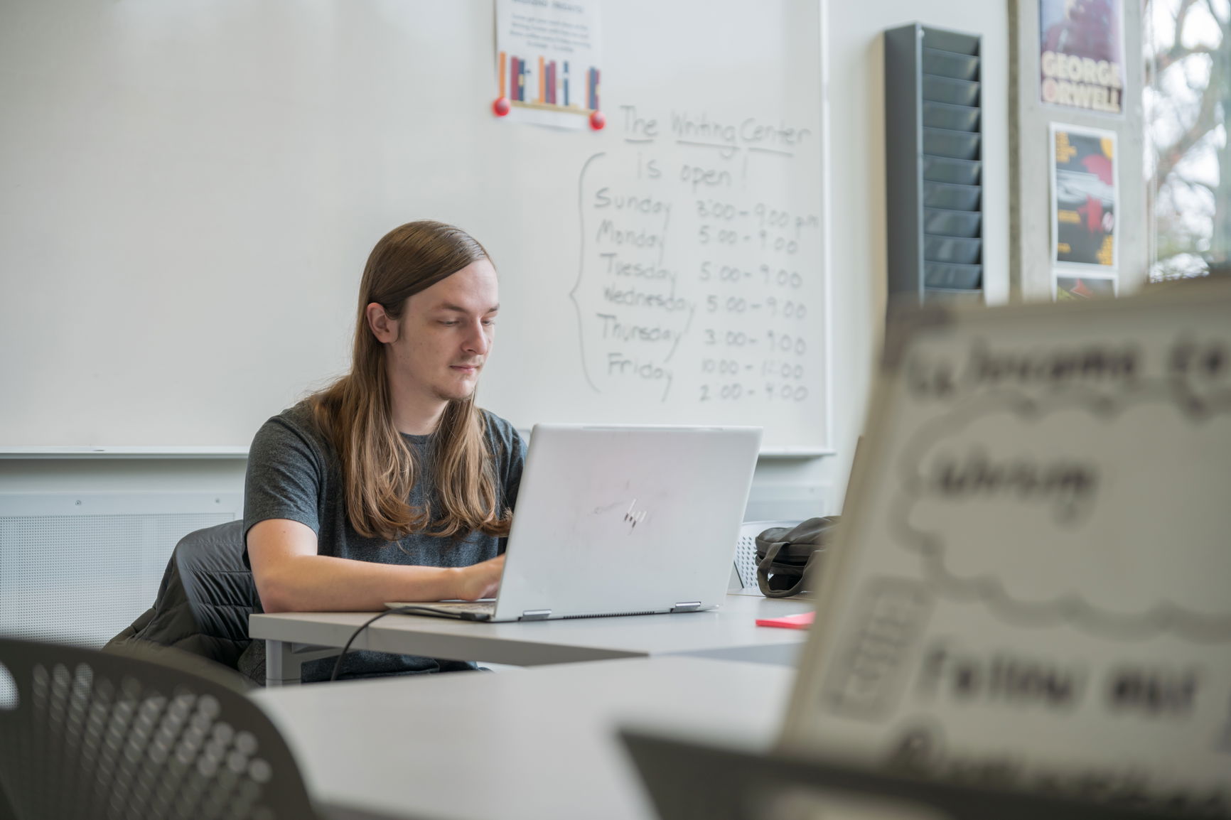 Person working on a laptop in a study room with a whiteboard in the background.