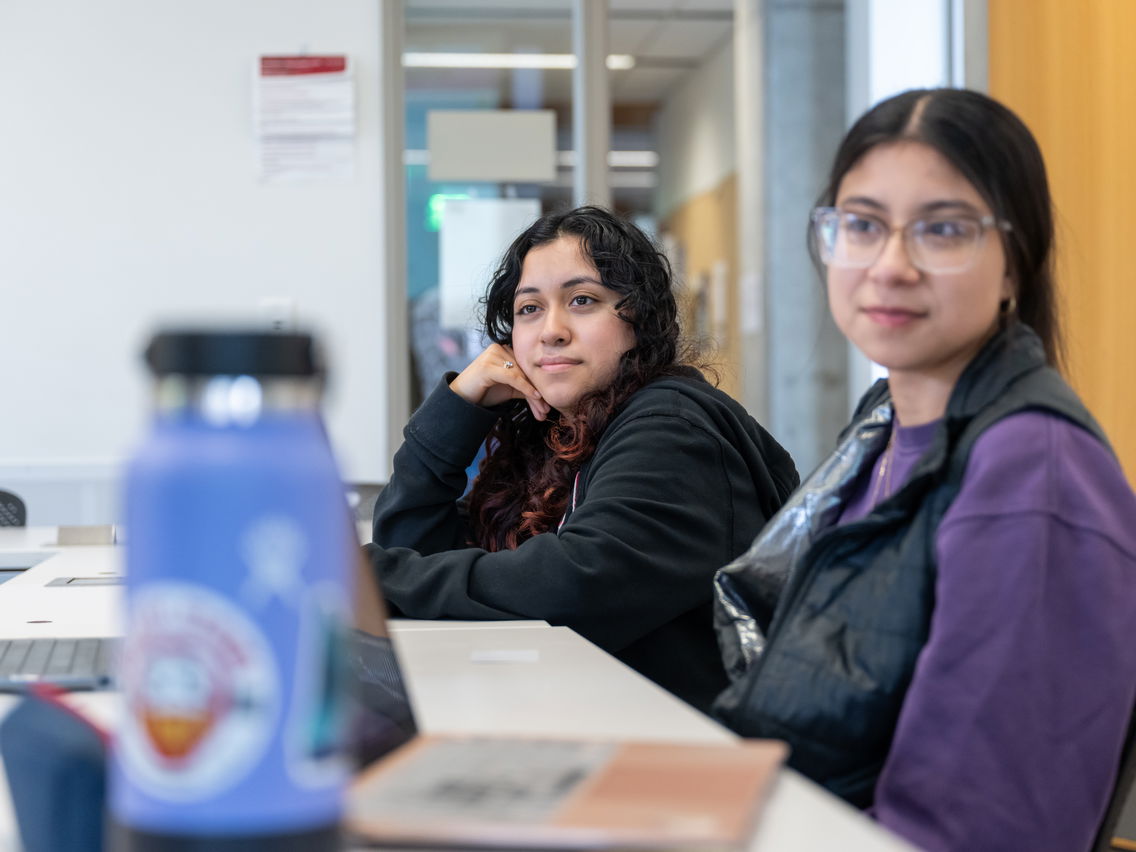 Two students sitting in class at a table. 