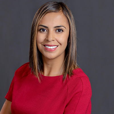 Professional portrait of a woman with shoulder-length light brown hair, wearing a red top, against a dark grey background.