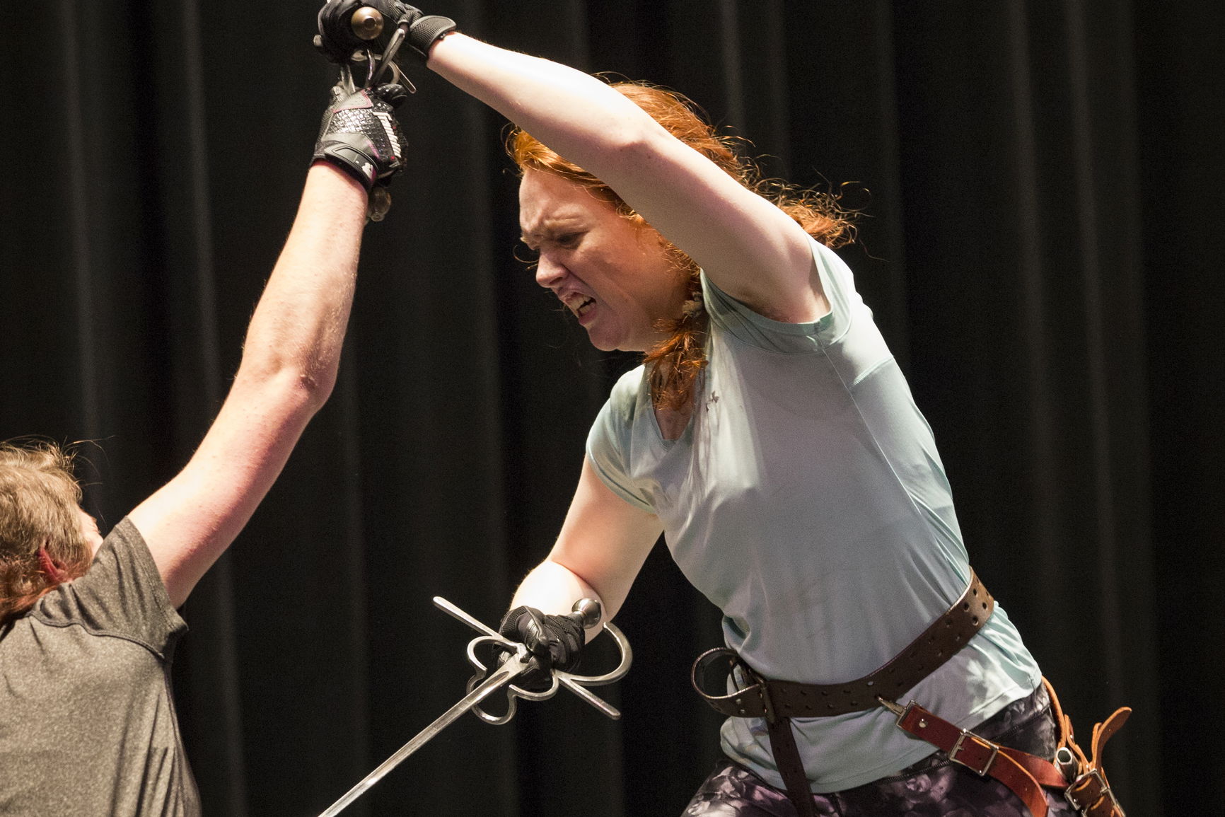 Two individuals engaged in intense fencing, both holding swords, with a dark background.