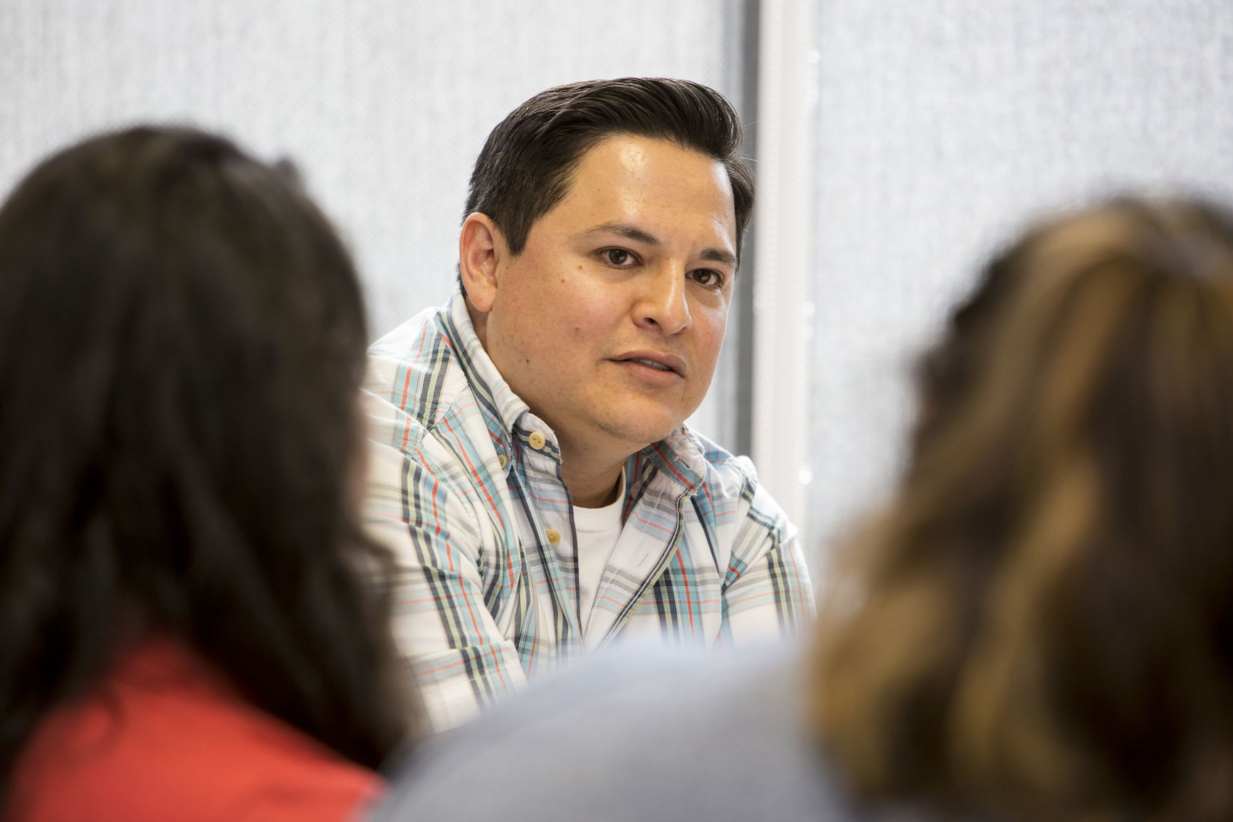 Man in a plaid shirt speaking to others in a room.