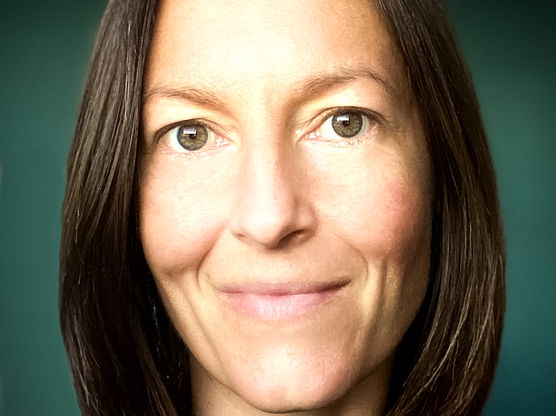 Close-up portrait of a person with shoulder-length dark brown hair and green eyes, smiling gently.