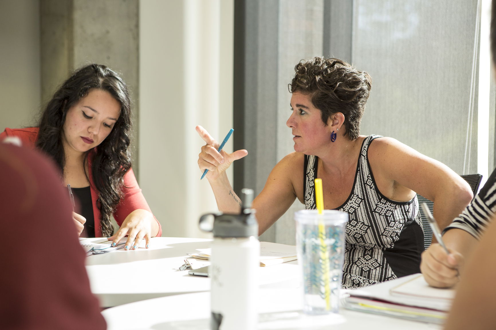 Two women having a discussion at a table with notebooks and water bottles.